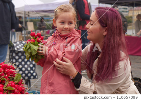 Young mother with little daughter buying fresh radishes 110657099