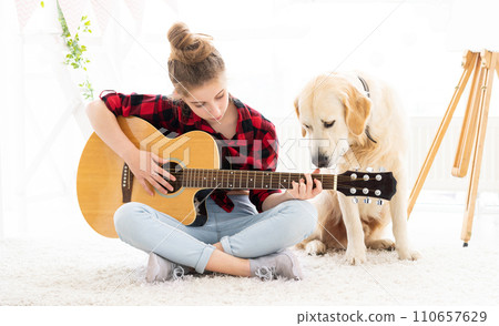 teenage girl playing guitar with cute dog at home 110657629