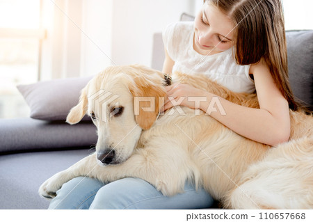 Sweet girl holding cute dog sitting on sofa indoors 110657668
