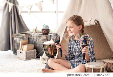 Smiling little girl with maracas in hands and ethnic drums on floor in children's room 110657830