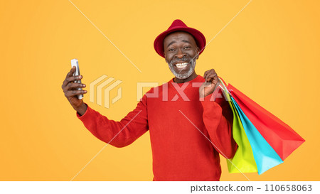 An ecstatic senior man in a red outfit and hat, taking a selfie with his phone An ecstatic senior man in a red outfit and hat, taking a selfie with his phone 110658063