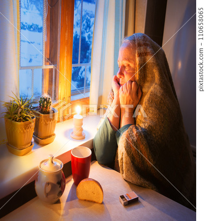 Woman warming herself by a candle in blackout 110658065