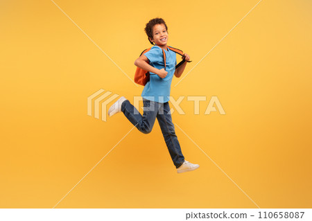 Joyful boy jumping with backpack on vibrant yellow background Joyful boy jumping with backpack on vibrant yellow background 110658087