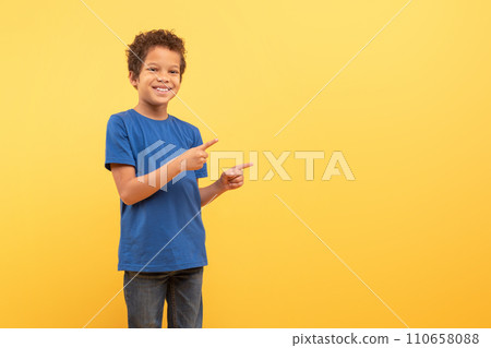 Boy pointing sideways at free space on yellow background Boy pointing sideways at free space on yellow background 110658088