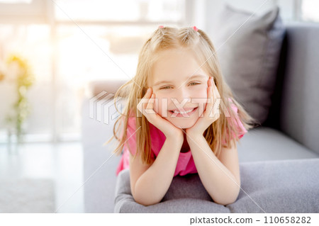 Happy little girl resting on sofa with head on hands indoors 110658282