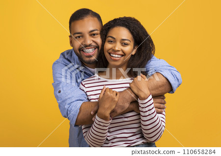 Loving black couple hugging with genuine smiles and looking at camera Loving black couple hugging with genuine smiles and looking at camera 110658284