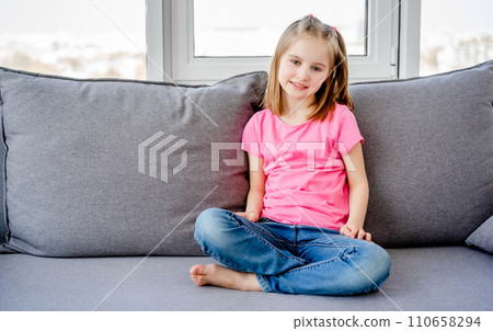 Cute litle girl sitting on grey sofa in light room Cute litle girl sitting on grey sofa in light room 110658294