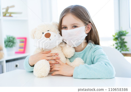 Little girl with plush teddy wearing medical masks at home 110658386