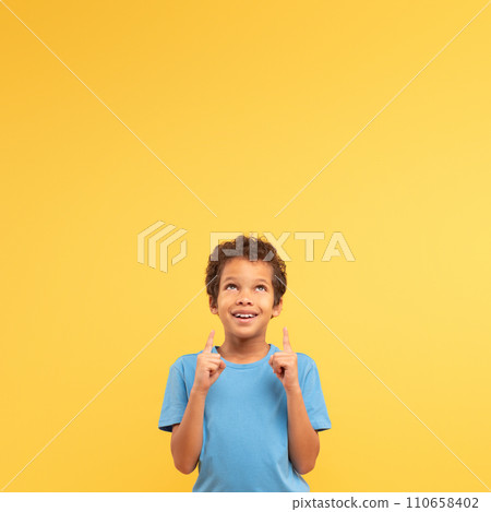Optimistic boy pointing up, hopeful on yellow square background 110658402