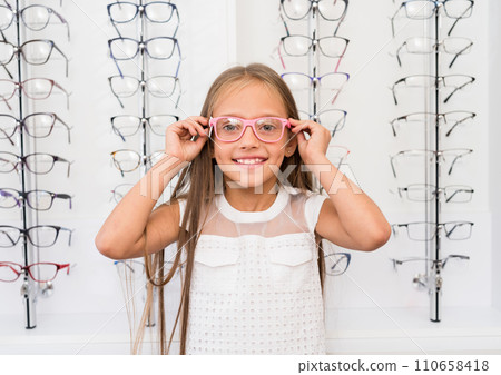 Little girl with a glasses standing in the optical store Little girl with a glasses standing in the optical store 110658418