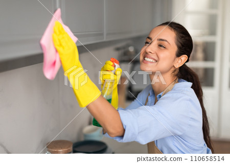 Smiling young woman in gloves cleaning glass with cloth Smiling young woman in gloves cleaning glass with cloth 110658514