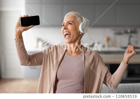 senior woman with headset and phone dancing and singing indoor senior woman with headset and phone dancing and singing indoor 110658519