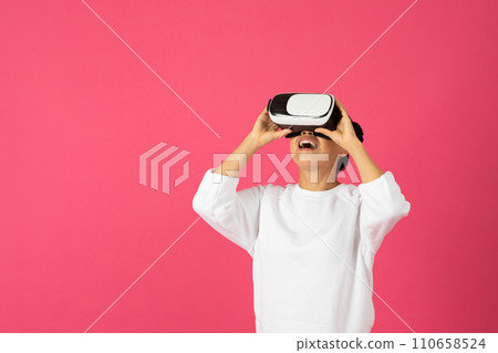 Excited Asian woman wearing VR headset, looking upwards with joyful expression Excited Asian woman wearing VR headset, looking upwards with joyful expression 110658524