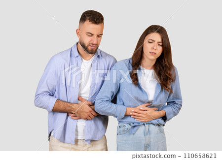 Couple with stomach ache, grimacing in discomfort on neutral background Couple with stomach ache, grimacing in discomfort on neutral background 110658621