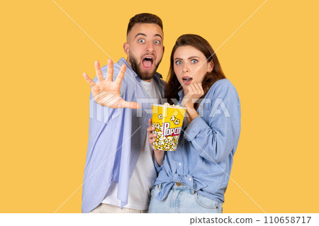 Couple with popcorn looking shocked, yellow background Couple with popcorn looking shocked, yellow background 110658717