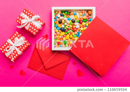 Red envelope with candy and gift box and Valentines hearts on colored background. Flat lay, top view. Romantic love letter for Holiday concept 110659504