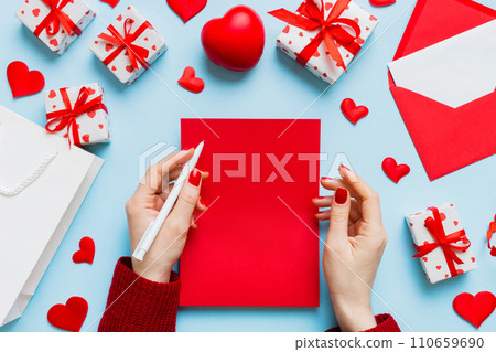 top view photo of valentine day decor female hands holding letter with envelope, small gift box and heart decoration on isolated pastel colored background with empty space 110659690