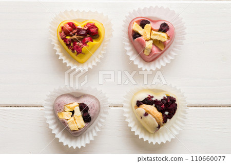 chocolate sweets in the form of a heart with fruits and nuts on a colored background. top view with space for text, holiday concept chocolate sweets in the form of a heart with fruits and nuts on a colored background. top view with space for text, holiday concept 110660077