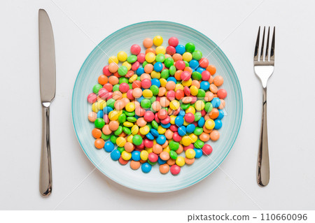 cutlery on table and sweet plate of candy. Health and obesity concept, top view on colored background 110660096