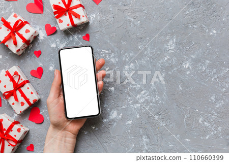 Woman hand holding mobile phone with blank screen on colored background with hearts, valentine day concept top view flat lay 110660399