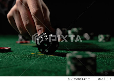 Close up of male hand rolling the dice on green poker table with black background 110661927