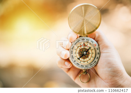 Close-up of hand holding a compass in the midst of a green forest offering ample space for text. Symbolizing guidance and exploration it relates to travel lifestyle and successful business management. 110662417