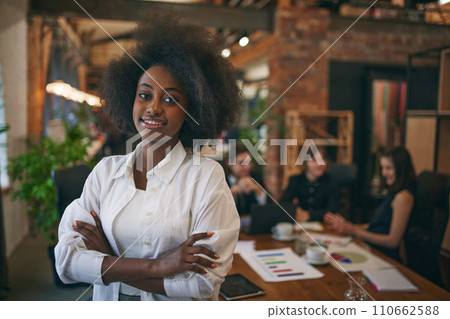 Portrait of African-American woman smiling at camera while classmates studying with laptop on background. Public library. 110662588