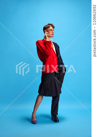 Duet of masculine and feminine voices. Full-length portrait of young attractive male model with female and male make-up talking on phone. 110662692