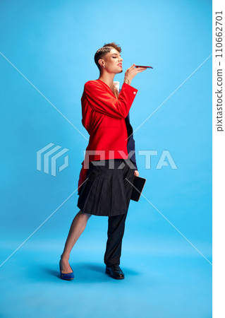 Dual faces of progressive leadership. Male model with masculine and feminine appearance talking on phone against blue background. Concept of connect. Dual faces of progressive leadership. Male model with masculine and feminine appearance talking on phone against blue background. Concept of connect. 110662701