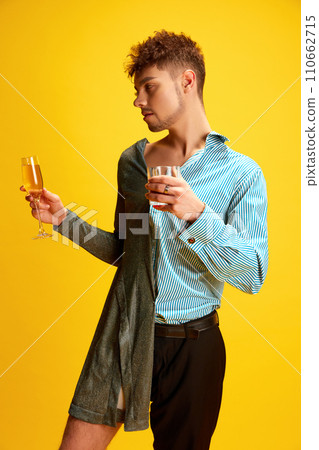 Bachelor and bachelorette party. Man half-wearing in woman's and man's clothes posing holding glasses of champagne and whiskey in hands. Bachelor and bachelorette party. Man half-wearing in woman's and man's clothes posing holding glasses of champagne and whiskey in hands. 110662715