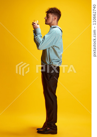Side view portrait of male model dressed as man and woman in unity drinking alcohol shot against yellow studio background. 110662740