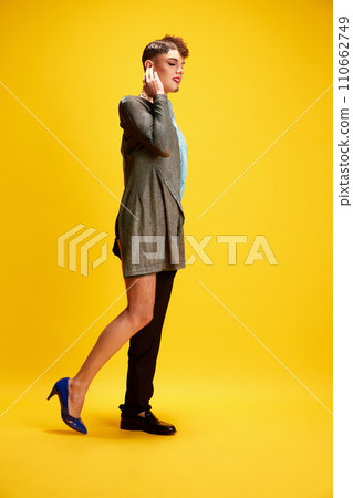 Masculine and Feminine Charm. Male model with make up of woman and man wearing in dress and smart casual outfit posing against yellow background. 110662749