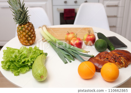 Home cooking on domestic kitchen table adorned with variety of organic ingredients including zucchini pineapple orange lettuce apple leek ready for delicious and nutritious preparation. 110662865