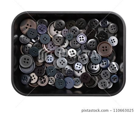 Plastic sew-through buttons, in a black plastic dish. Flat buttons with holes through which thread is sewn to attach the button. Fastener that joins two pieces of fabric together. Close-up from above. 110663025