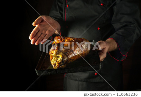 Baked duck carcass on a baking sheet in the hands of a chef. Concept of cooking delicious poultry. Dark space for advertising Baked duck carcass on a baking sheet in the hands of a chef. Concept of cooking delicious poultry. Dark space for advertising 110663236