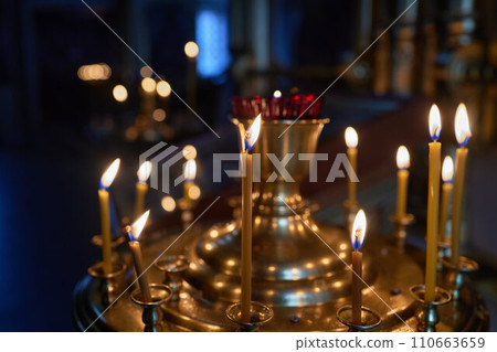 Burning church candles in a gilded candlestick in a temple in the dark Burning church candles in a gilded candlestick in a temple in the dark 110663659