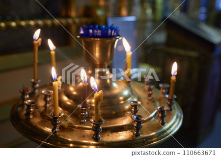 Burning church candles in a gilded candlestick in a temple in the dark Burning church candles in a gilded candlestick in a temple in the dark 110663671