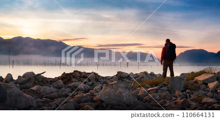 Adventure Man standing on rocky shore by the lake with mountains in background. 3d Rendering. 110664131