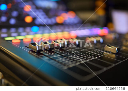 An expert adjusting audio mixing console with white blank screen laptop on control desk. An expert adjusting audio mixing console with white blank screen laptop on control desk. 110664236