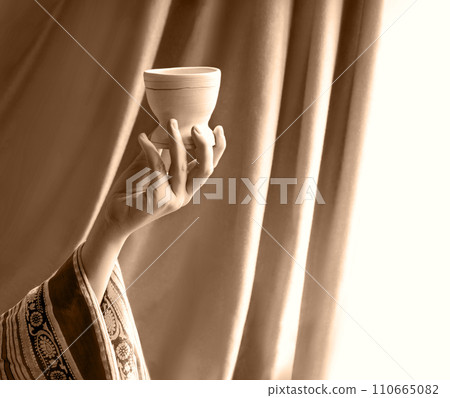 A hand in ancient clothing holds a clay bowl 110665082