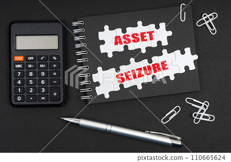 On the table is a calculator, a pen and a notebook with the inscription - Asset Seizure 110665624