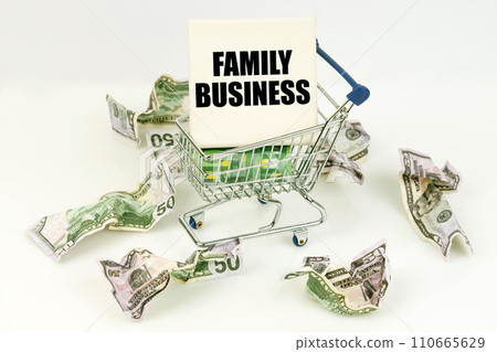 Crumpled dollars lie on a white surface, there is a cart inside a sign with the inscription - FAMILY BUSINESS Crumpled dollars lie on a white surface, there is a cart inside a sign with the inscription - FAMILY BUSINESS 110665629