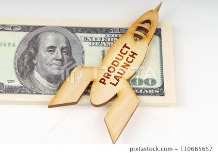On the dollars lies a wooden model of a rocket with the inscription - Product Launch On the dollars lies a wooden model of a rocket with the inscription - Product Launch 110665657