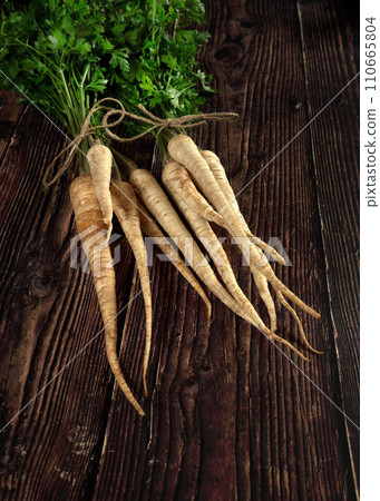 Bunch of parsley roots with green leaves on dark wooden board Bunch of parsley roots with green leaves on dark wooden board 110665804