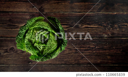Top down view, single raw savoy kale cabbage on dark wooden board, wide banner space for text right side 110665839