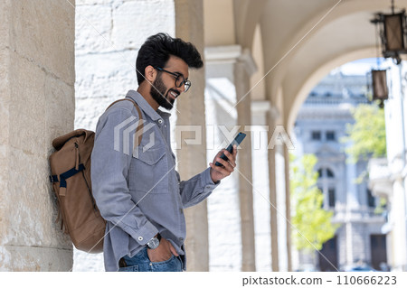 Smiling dark-haired man standing in the arch with a phone in hand Smiling dark-haired man standing in the arch with a phone in hand 110666223