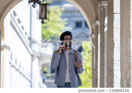 Dark-haired man walking through the arch and talking on the phone Dark-haired man walking through the arch and talking on the phone 110666228