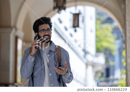 Dark-haired man walking through the arch and talking on the phone Dark-haired man walking through the arch and talking on the phone 110666229