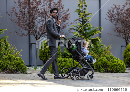 Dark-haired young businessman with a baby carriage outside 110666516