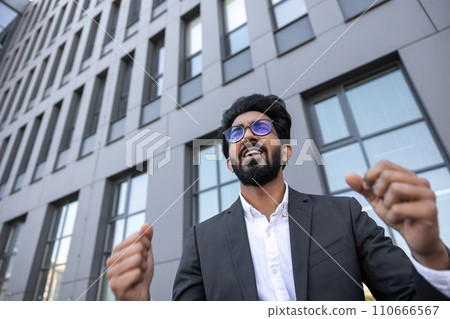 Waist up of an excited successful hindu businessman near the office building Waist up of an excited successful hindu businessman near the office building 110666567